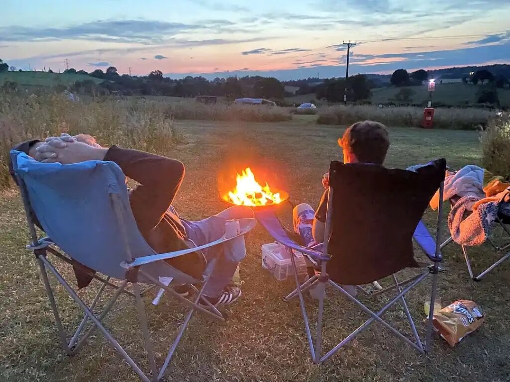 2 People sat on camping chairs around a cosy camp fire as the sun sets